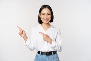 Image of smiling young office lady, asian business entrepreneur pointing fingers left, showing client info, chart of banner aside on copy space, white background photo