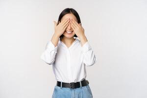 Image of young asian woman close her eyes and smiles, waits for surprise, anticipates, stands over white background photo