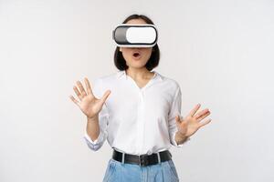 Amazed young woman in virtual reality, using vr glasses headset, standing over white background photo