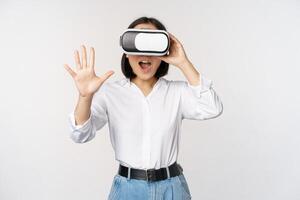Vr chat. Asian girl saying hello in virtual reality glasses, smiling enthusiastic, concept of communication and future technology, white background photo
