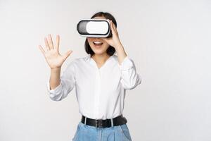 Vr chat. Asian girl saying hello in virtual reality glasses, smiling enthusiastic, concept of communication and future technology, white background photo