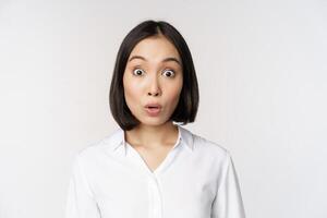 Close up portrait of young asian female model looking amazed at camera, smiling white teeth, standing against white background photo