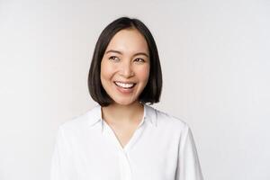 Image of smiling asian woman planning, thinking of smth, daydreaming, standing over white background with smug face photo