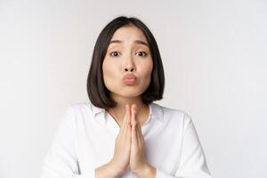 Cute asian woman begging, say please, asking for favour, need help, standing with coy face against white background photo