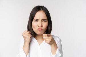 Close up of angry young woman clench fists, ready for fight, fighting, standing over white background photo