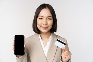 Smiling corporate woman in suit, showing mobile phone screen and app on mobile phone, smartphone screen, standing over white background photo