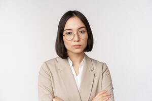 Professional asian businesswoman in glasses, looking confident at camera, standing in power pose against white background photo