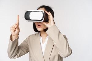 Amazed business woman in suit using virtual reality glasses, looking amazed in vr headset, standing over white background photo