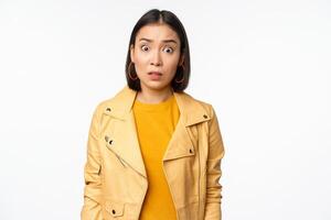 Image of shocked, confused asian woman, staring frustrated and speechless at camera, raising eyebrows and looking concerned, standing over white background photo