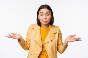 Image of korean girl shrugs shoulders and looks confused, dont know, cant tell, standing over puzzled over white background photo