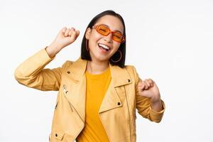 Happy stylish korean girl in sunglasses, dancing and laughing, smiling carefree, standing over white background photo