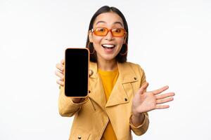 Enthusiastic asian female model, showing smartphone app interface, online store or website on mobile phone screen, standing over white background photo