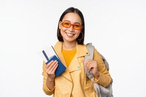 contento asiático niña yendo en vacaciones, participación pasaporte y vuelo Entradas, mochila en hombro. joven mujer turista de viaje en el extranjero, en pie terminado blanco antecedentes foto