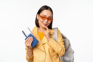 Asian girl tourist with boarding tickets and passport going abroad, holding backpack, thinking of travelling, standing over white background photo