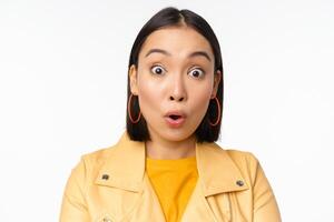 Close up of impressed asian girl, say wow, looking amazed at camera, standing in casual clothes over white background photo