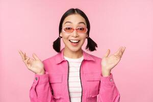 Image of asian girl looking surprised and excited, smiling, amazed reaction to big news, standing over pink background photo