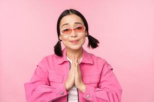 Please. Cute asian girl asking favour, begging, standing against studio background photo