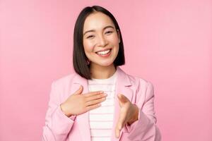 Portrait of smiling, pleasant businesswoman shaking hands with business partner, handshake, extending hand and saying hello, standing over pink background photo