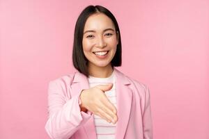 Portrait of smiling, pleasant businesswoman shaking hands with business partner, handshake, extending hand and saying hello, standing over pink background photo