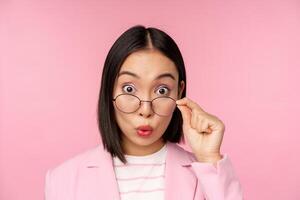 Close up portrait of korean office lady takes off glasses and looking impressed at camera, surprised face expression, pink background photo