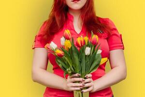 Young woman holds large bouquet of tulips in her hands on yellow background. photo