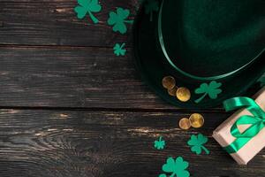 Leprechaun hat, gold coins, clover shamrock and green ribbon gift on dark wooden background. Good luck symbols for St. Patrick's Day. photo