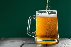 Beer is pouring into a mug on a green background. Celebrating St. Patrick's Day. Traditional Irish drink. photo