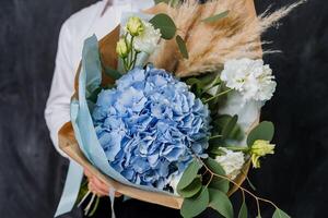 A girl in a white shirt holds a large bouquet with blue hydrangea and other flowers. The bouquet is wrapped in colored paper. Gift for the teacher for the first of September. photo