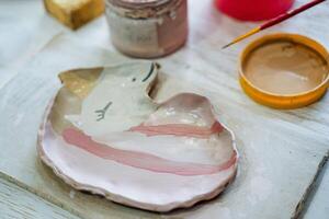 un plato de arcilla en el forma de un unicornio con un rosado melena mentiras en el mesa, siguiente a el pintar y cepillar. creatividad en el cerámica taller. foto