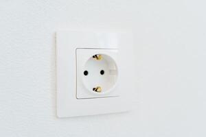 Socket made in a white wall. Socket with grounding. Electricity in the house. A close shot of interior elements. photo