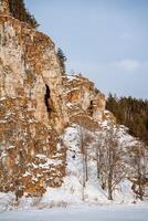 invierno paisaje de un rock en el banco de el río. el rocoso montañas de naranja color son esparcido con nieve. frío ruso invierno. ural montañas foto