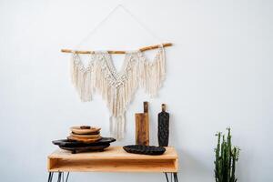 there is a table in the middle of the frame. There are several wooden plates and boards on it. In the right corner there is a pot with a cactus. A decorative pancho hangs above the table. photo