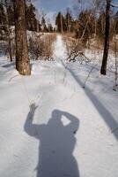 The shadow of a man in the snow on a sunny day. Raised hand up. Hiking through a snow-covered forest photo