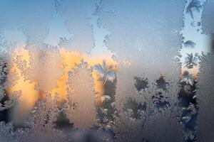 escarchado modelo en el ventana, puesta de sol rayos pasar mediante el vaso. un raro natural fenómeno en invierno. dibujo de congelado agua foto