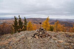 On the mountain lies a bunch of stones collected in a hill with a sign. Mountain landscape with panoramic views of the surroundings, obese clouds fly low over the horizon, dull autumn time. photo