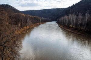 A wide river between the mountains, the shore is covered with autumn golden forest. The onset of autumn and cold. photo