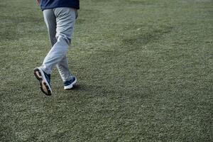 A man runs across a green football field in sportswear. Sports and playing football. Active training, strengthening of muscles and skeleton. photo