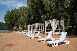 White sunbeds are placed on the sandy shore under the sun and tents are installed in the shade. photo