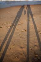 Long shadows on the sandy shore. A couple in love walks along the beach, holding hands. Relax by the sea, sea breeze and warm sand photo