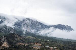 Atmospheric view of the mountain forest, the tops of the mountains are covered with descending fog. At the bottom of the plain settlement. Mesmerizing mountain views, the beauty of wildlife photo