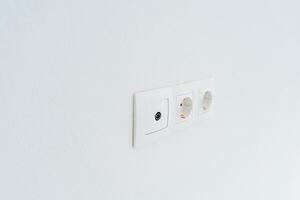 Triple white socket with a switch on the wall. Electricity in the house. Minimalistic interior of a modern house. photo