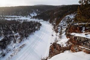 Winter view from the cliff to the river valley. A cold January landscape. Frozen river at the foot of the rocky mountains photo