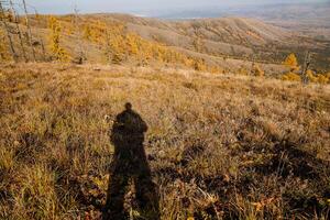 A man is standing on the slope of a hill. The sun is shining brightly. The time of the year is autumn. Several more ridges are visible ahead photo