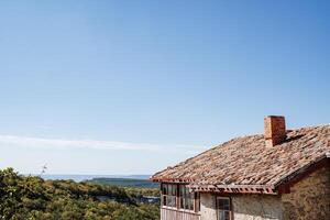 Old house with a tiled roof in the mountains. Clear endless sky, view of the green plains. Rest at the resort. Antique house. photo