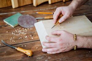 the hands of the master cut a drawing on a wooden board. the carpenter works with wood. tool for creativity and artistic cutting photo