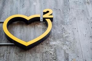 Street decoration in the form of a heart. A large yellow sign in the shape of a heart with the number two hangs on a concrete wall. Art Square City Park. photo