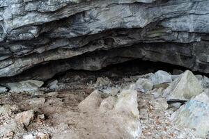 a stone entrance to the cave. karst failure in the ground. dark black hole deep in the cave. mountainous terrain. winter in the mountains. photo