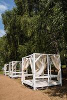 White exquisite tents are installed in the shade of trees on the sandy shore. There's no one around. photo