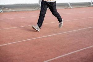 un cerca Disparo de un hombre corriendo en el corriendo carril. trotar en un Deportes uniforme mediante el estadio. activo descansar, capacitación, fortalecimiento de el cuerpo y inmunidad con el ayuda de físico cultura. foto