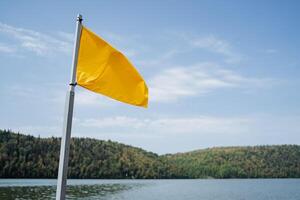 A bright yellow flag flies over the water. In the background are green mountains. photo